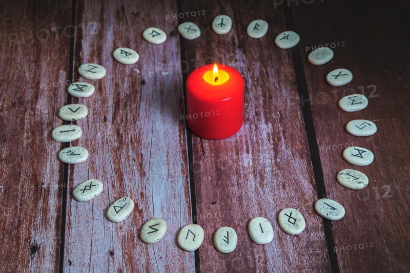 Circle of Viking stone runes on a wooden table with a lighted red candle in the center