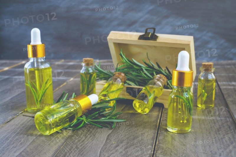Close-up of a dropper with a drop of rosemary oil in the background several bottles of rosemary essence in a wooden box