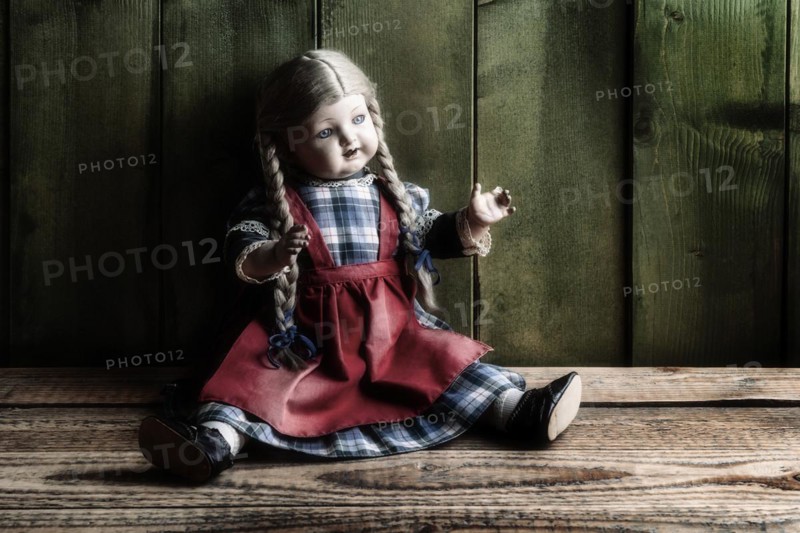 Antique porcelain doll on rustic board floor in front of green wooden wall