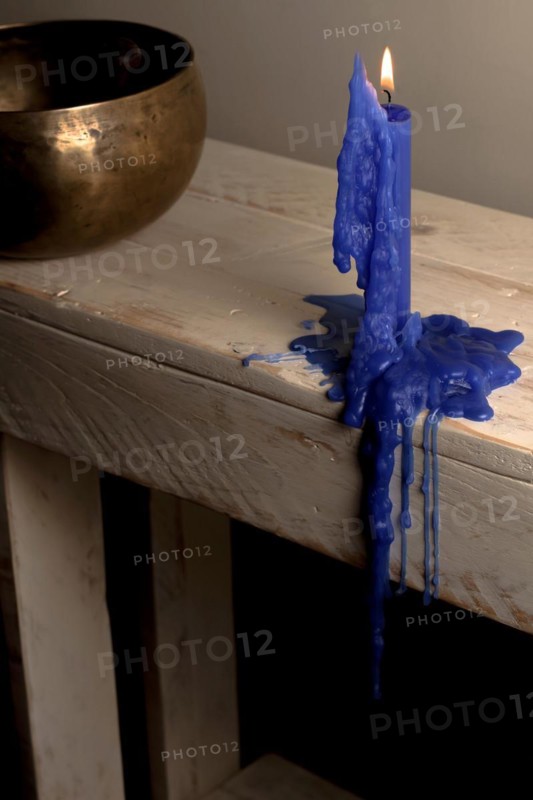 Lighted blue candle melted on a wooden table with a Tibetan bowl in the background