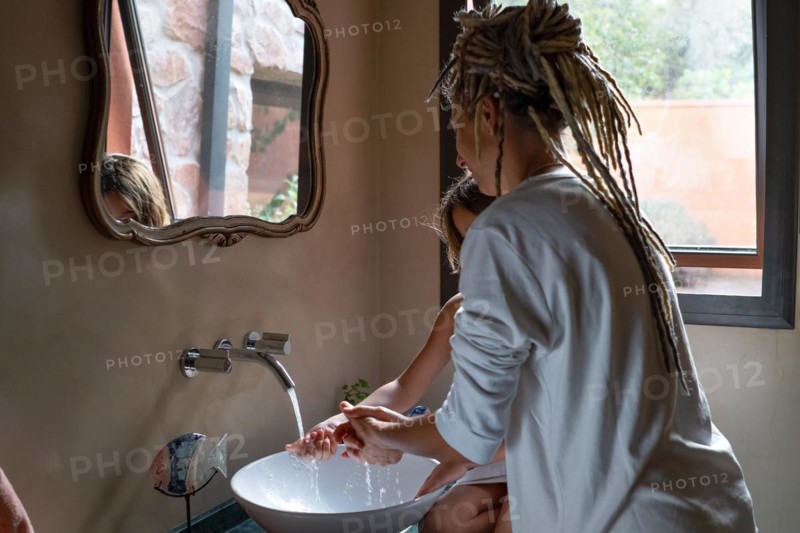 Mother and daughter wash their hand together in the bathroom sink. Design bathroom. Motherhood concept