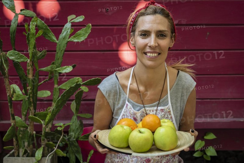 A woman carring a plateb full of fresh citrus and apples