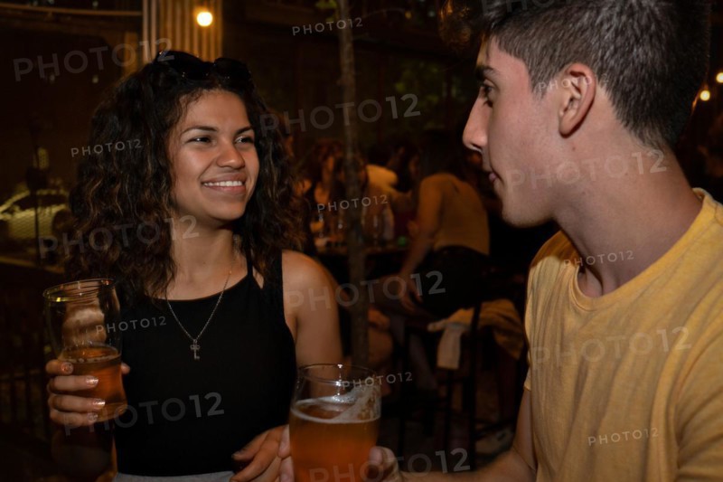 Young latina woman smiling and chatting with a young man in a bar drinking beer. Meeting of an online date. Blurred background