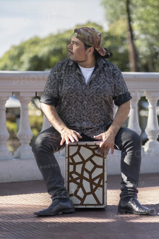 Hispanic man shot hands playing percussion with a Flamenco box sitting on top of it in a park