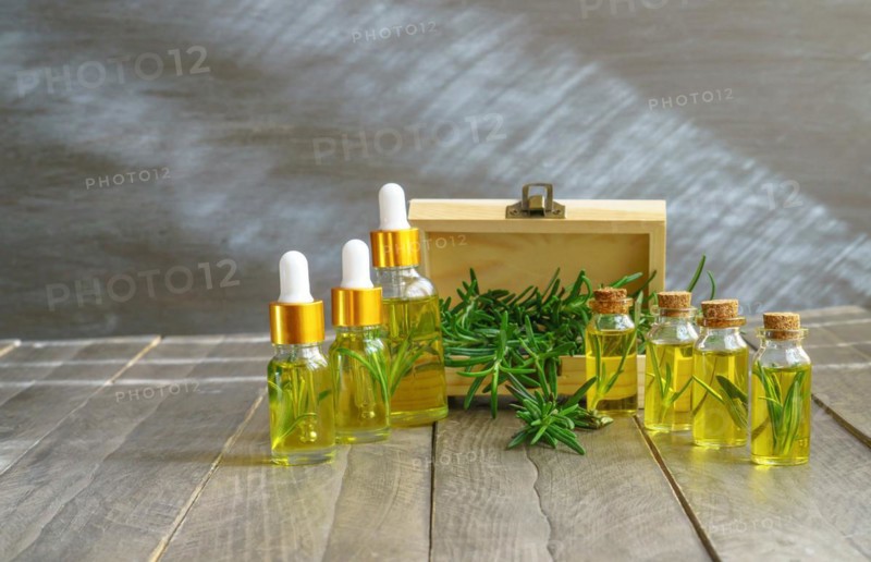 Bottles in a row with droppers of rosemary essential oil with a wooden box and fresh rosemary branches