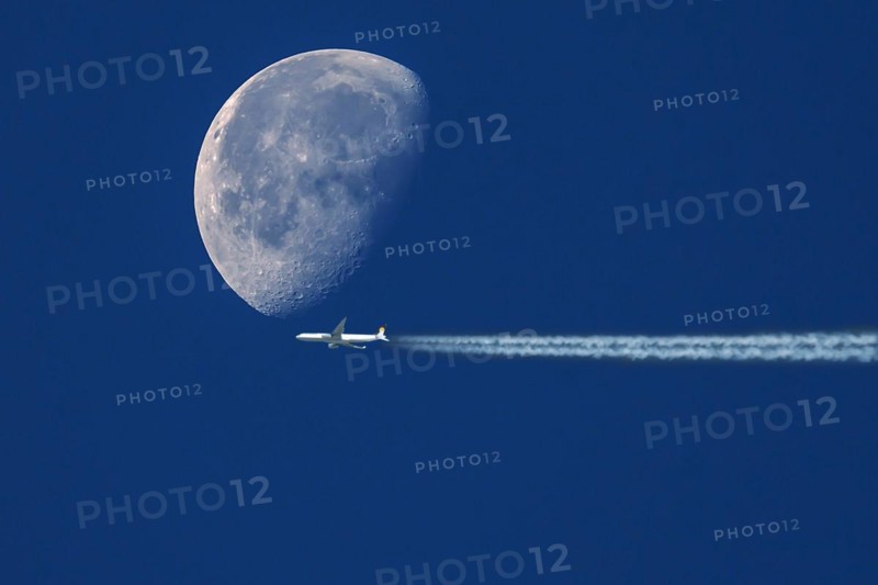 Plane with contrails in front of waning moon in early morning sky