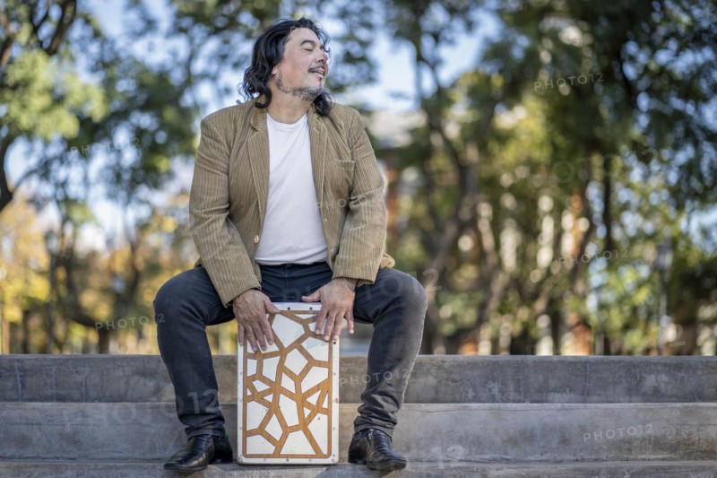 Hispanic man shot hands playing percussion with a Flamenco box sitting on top of it in a park