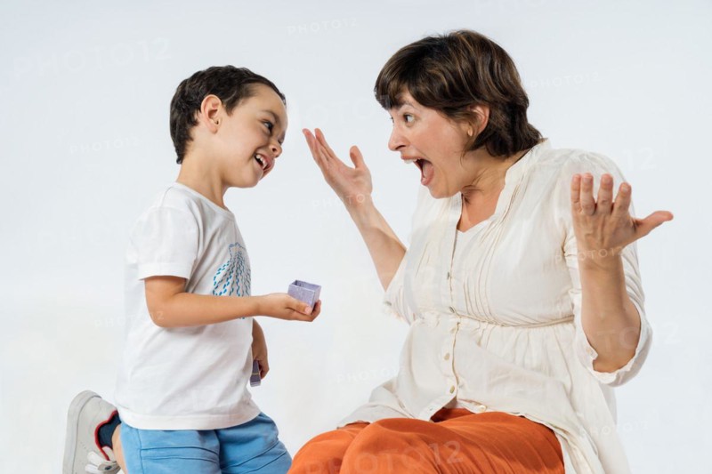 A little boy surprises his mother with a gift. Mother's day concept. Mum's birthday. Studio image with white background