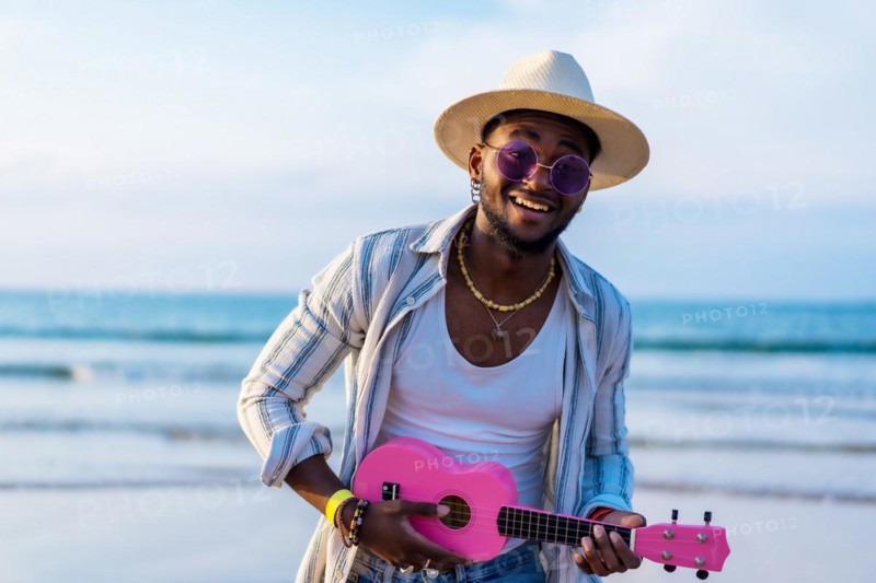Black ethnic man playing ukulele by the sea enjoying summer vacation on the beach