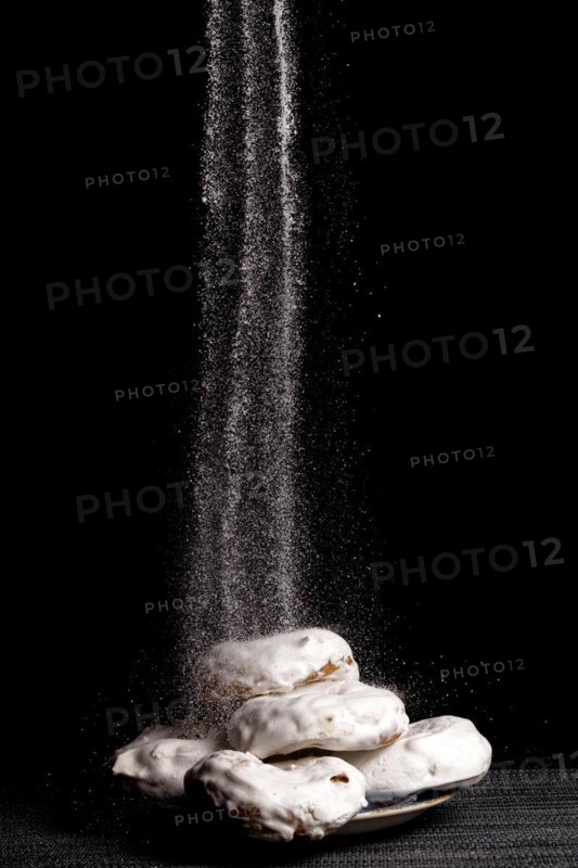 Glazed sugar doughnuts with icing sugar falling on them with black background and copy space
