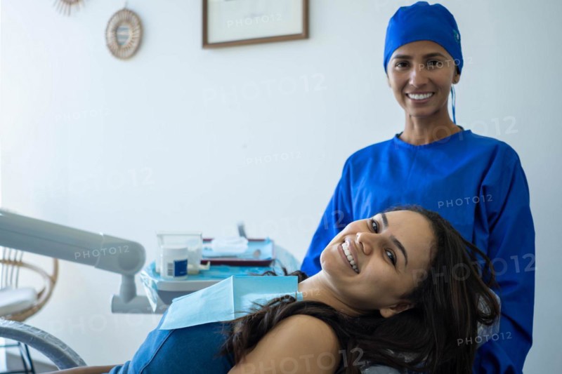 Beautiful young woman smiles sitting in the dentist's chair. She and her doctor look at the camera happy with the result of orthodontic treatment
