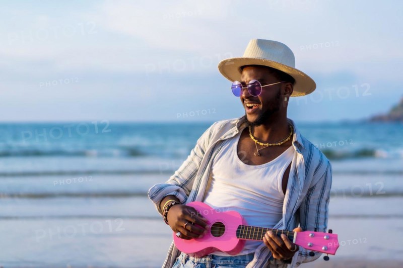 Portrait of black ethnic man enjoy summer vacation on the beach playing ukulele