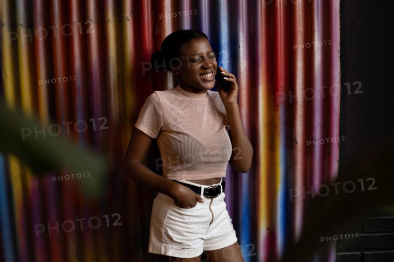 Smiling young african american woman talking with cellphone on wall of metal colors background