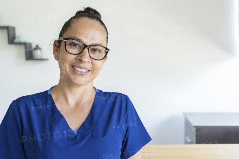 Woman in glasses wears a blue uniform looks at the camera smiling. Close up and copy space. Medical concept
