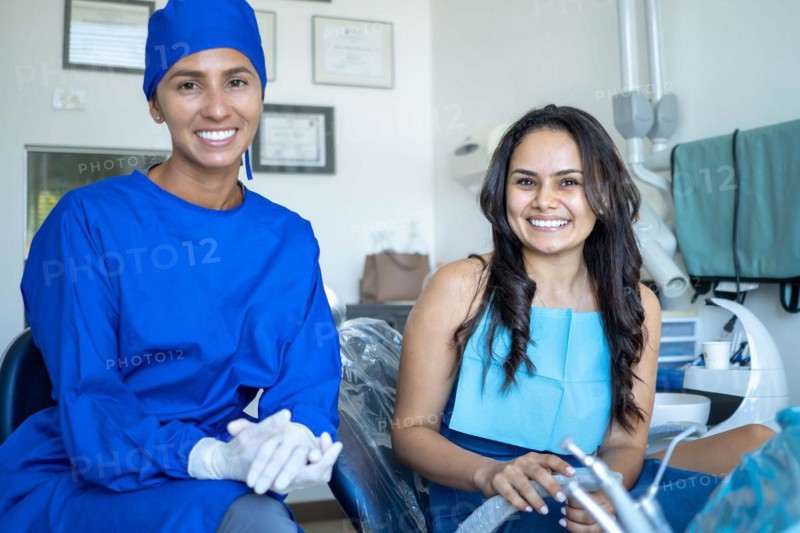 Smiling young woman in dental exam with her dentist both look at camera