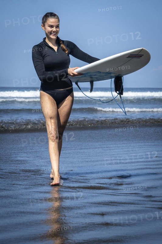 Young woman with prosthesis coming out of the sea with her surfboard. Concept of disability in sport