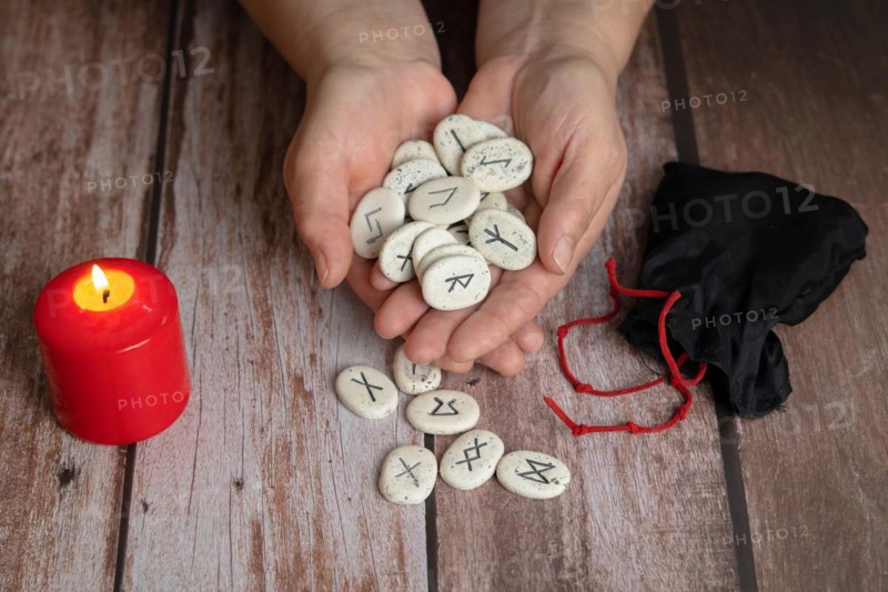 Woman reading the future with Viking runes with a red candle burning on a wooden table