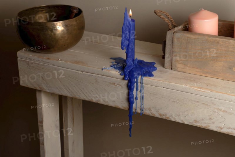 Lighted blue candle melted on a wooden table with a Tibetan bowl in the background and a wooden box with a pink candle