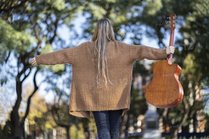 Guitarist in a park posing backwards holding his guitar with one hand