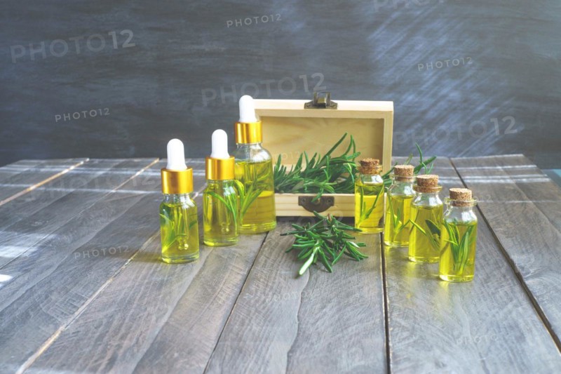 Bottles in a row with droppers of rosemary essential oil with a wooden box and fresh rosemary branches