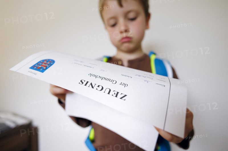 Symbolic photo on the subject of report cards in primary school. A boy poses with a report card. Berlin