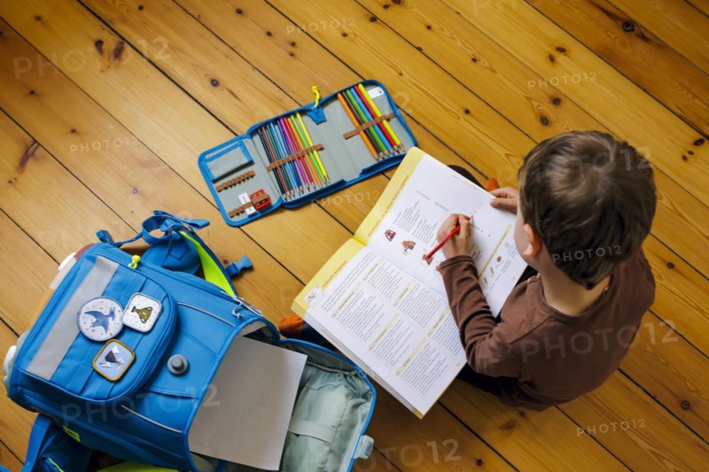 Symbolic photo on the subject of doing homework at home. A boy sits on the floor doing homework. Berlin