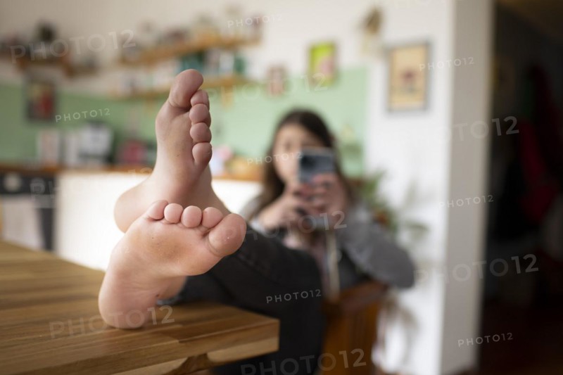 Subject: Girl sitting with feet on the table in the living room using a mobile phone