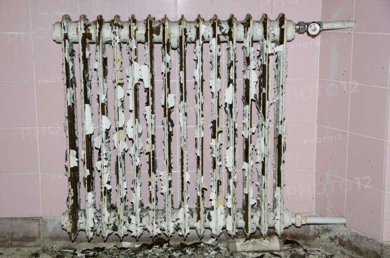 Old rusty radiator with pink tiles in background