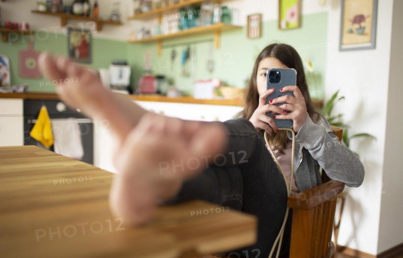 Subject: Girl sitting with feet on the table in the living room using a mobile phone