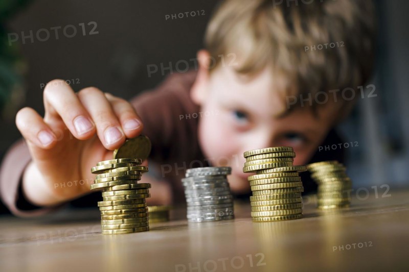 Symbolic photo on the subject of saving money in childhood. A five-year-old boy stacks small change on a table. Berlin