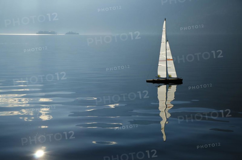 Sailing boat on an alpine lake Maggiore with Brissago islands and reflections in Ticino