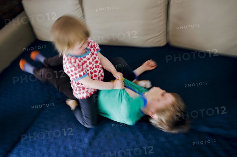 Symbolic photo on the subject of quarrels between siblings. A two-year-old girl and a five-year-old boy fight on a couch at home. Berlin