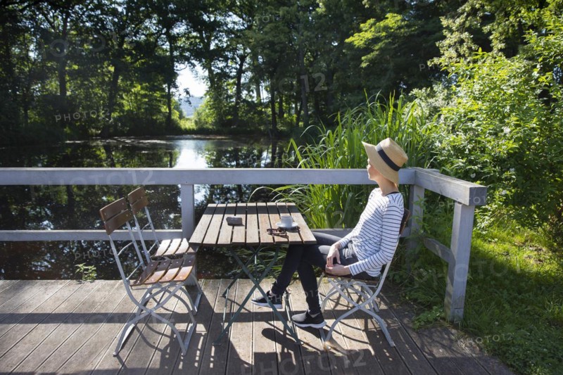 Woman sitting by a pond drinking coffee