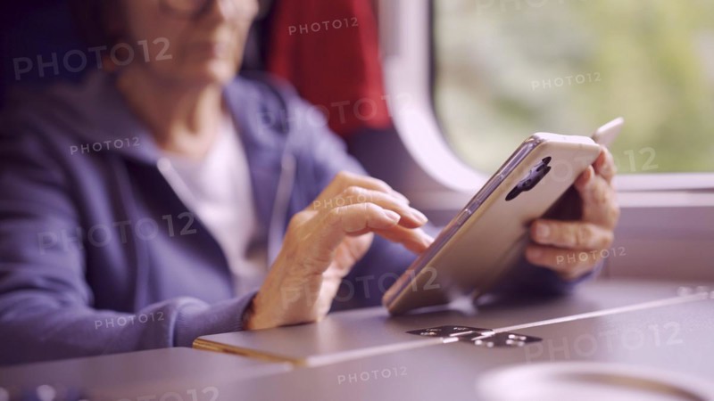 Close-up of the hands of an elderly woman sitting in a train carriageriage and using a smartphone