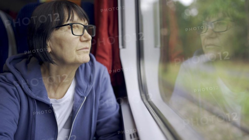 Elderly lady in glasses travels in train and looking out the window reflected in the glass