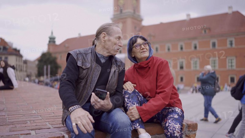 Elderly couple of tourists are sitting and talking in the historic center of an old European city