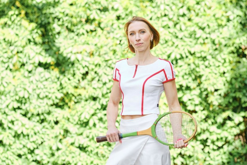 Adult redhead woman in tennis outfit posing with tennis racket