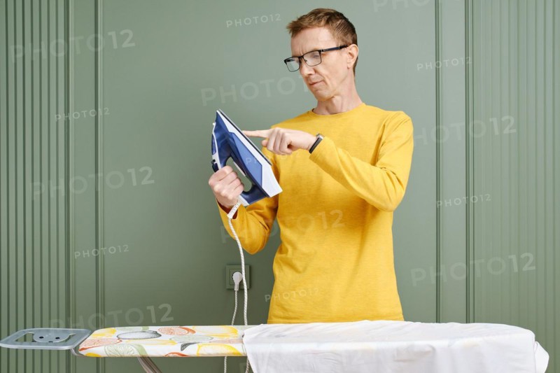 Middle aged man in spectacles touching the sole of an iron with finger