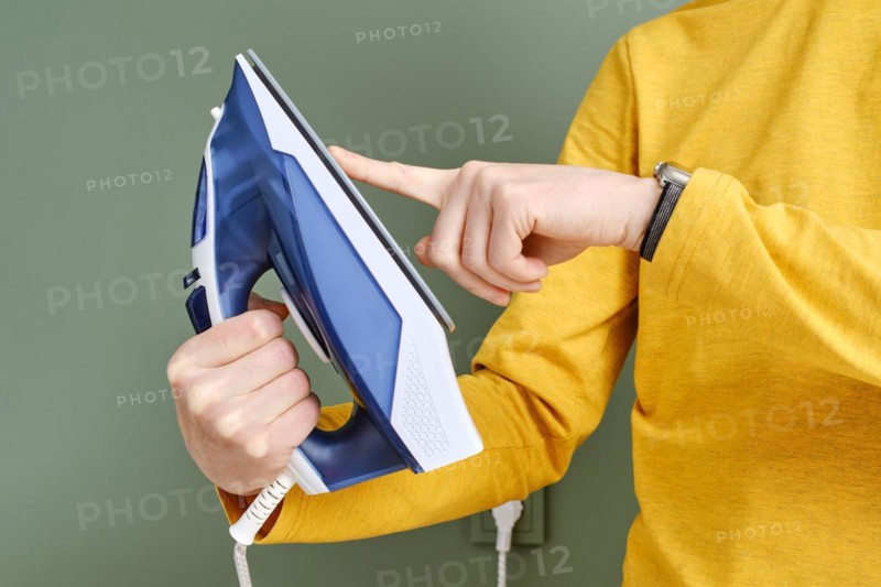 Unrecognizable man touching the sole of an iron with finger