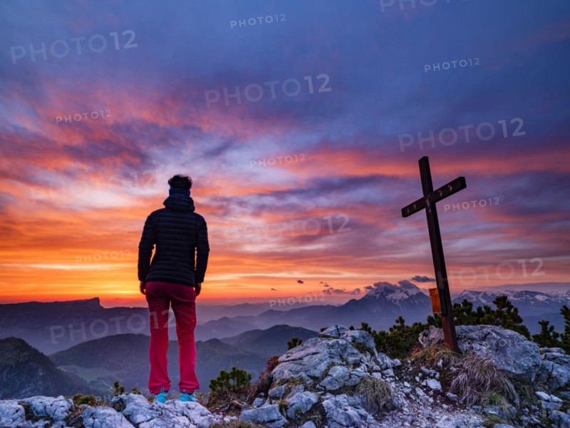 Mountaineer next to the summit cross of the iceberg and red clouds at dawn