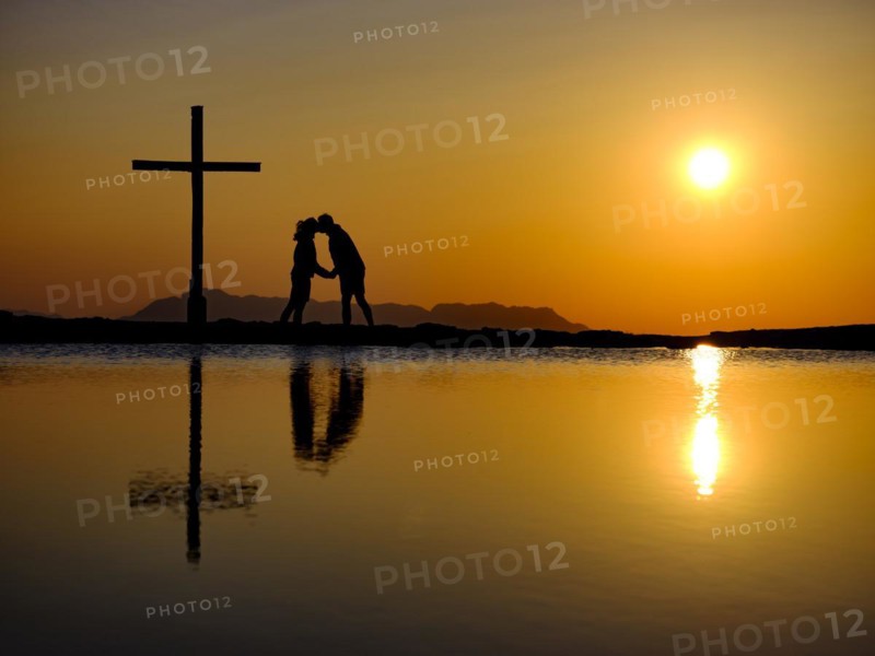Couple kissing next to summit cross at sunset