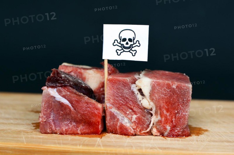 Chunks of raw meat on wooden plate with flag with poisonous skull sign