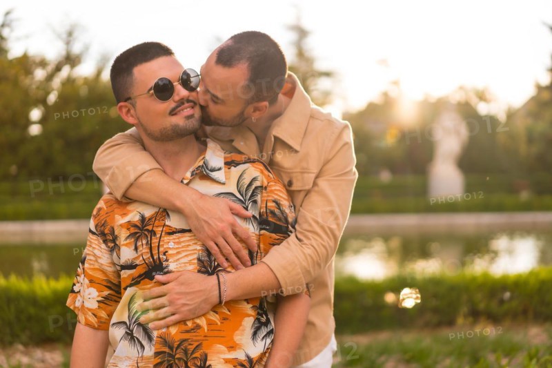 Homosexual couple embraced giving each other a kiss at sunset in a park in the city