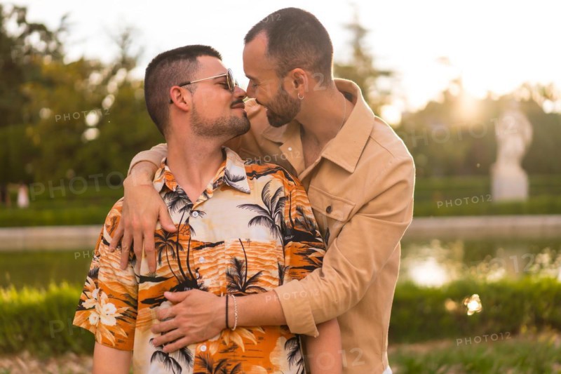 Homosexual couple embracing giving each other a kiss looking at the sunset in a park in the city