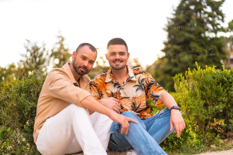 Romantic portrait of gay newlyweds sitting having fun at sunset in a park in the city