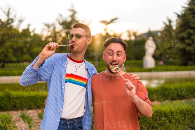 Portrait of laughing wedding couple eating a lollipop in the park on sunset in the city
