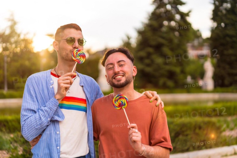 Portrait of laughing wedding couple eating a lollipop in the park on sunset in the city