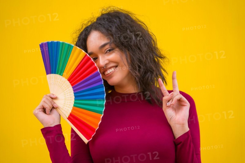 Portrait of a latin woman smiling with a rainbow lgbt fan on a yellow background