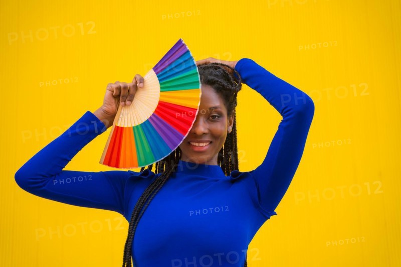 A black ethnic woman with a rainbow lgbt fan on a yellow background