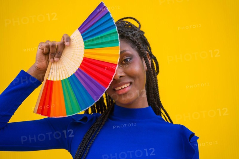 A black ethnic woman with a rainbow lgbt fan on a yellow background
